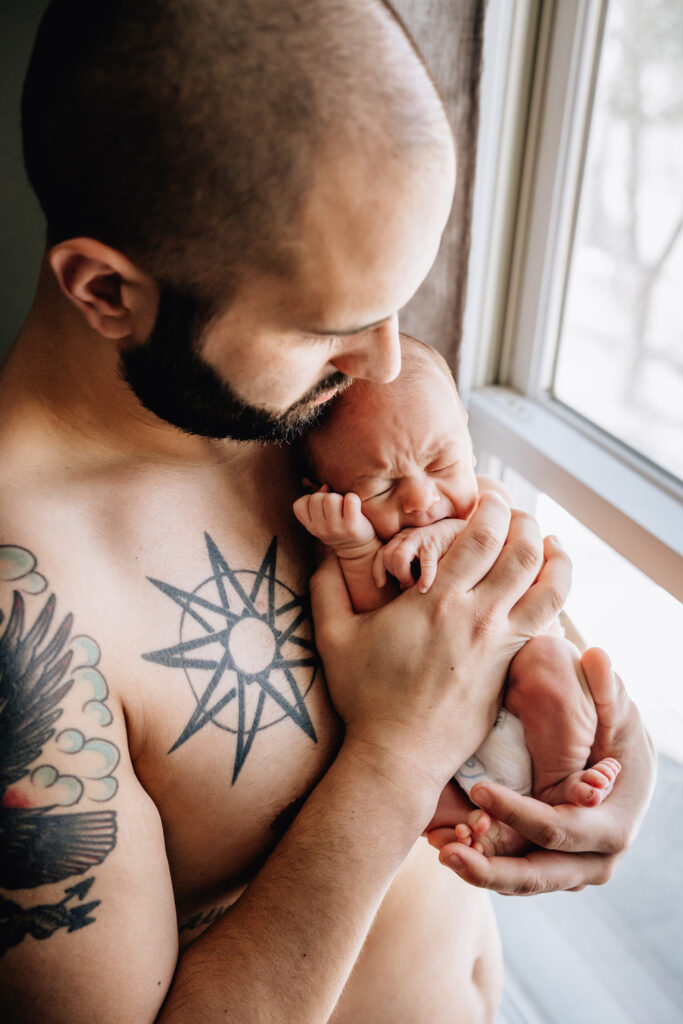 small newborn baby being held by parent bare chested