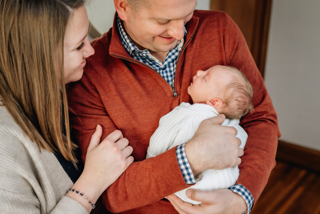 Mother and father smiling at new born baby in fathers arms