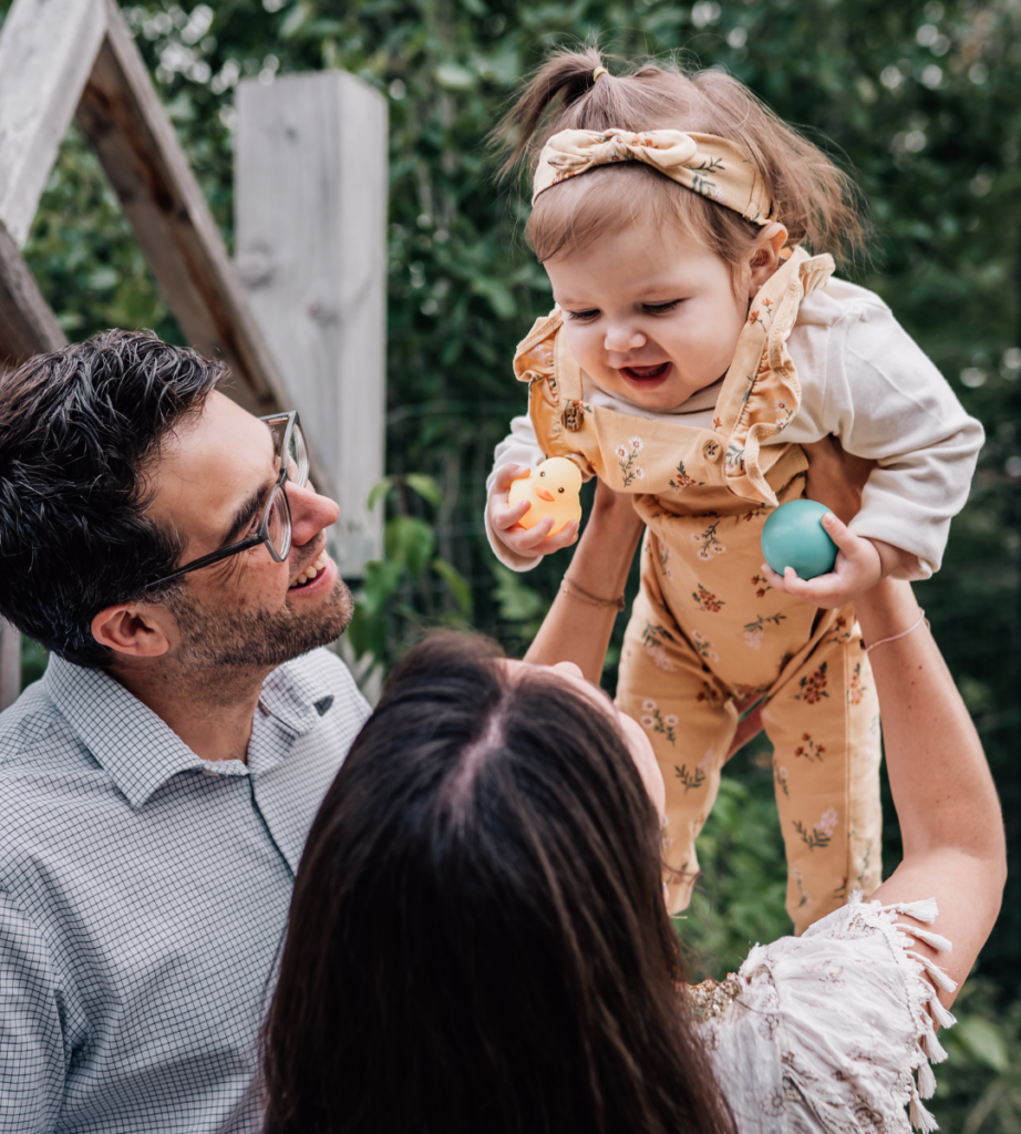 mother and father admiring their toddler who is holding a ball and rubber duck