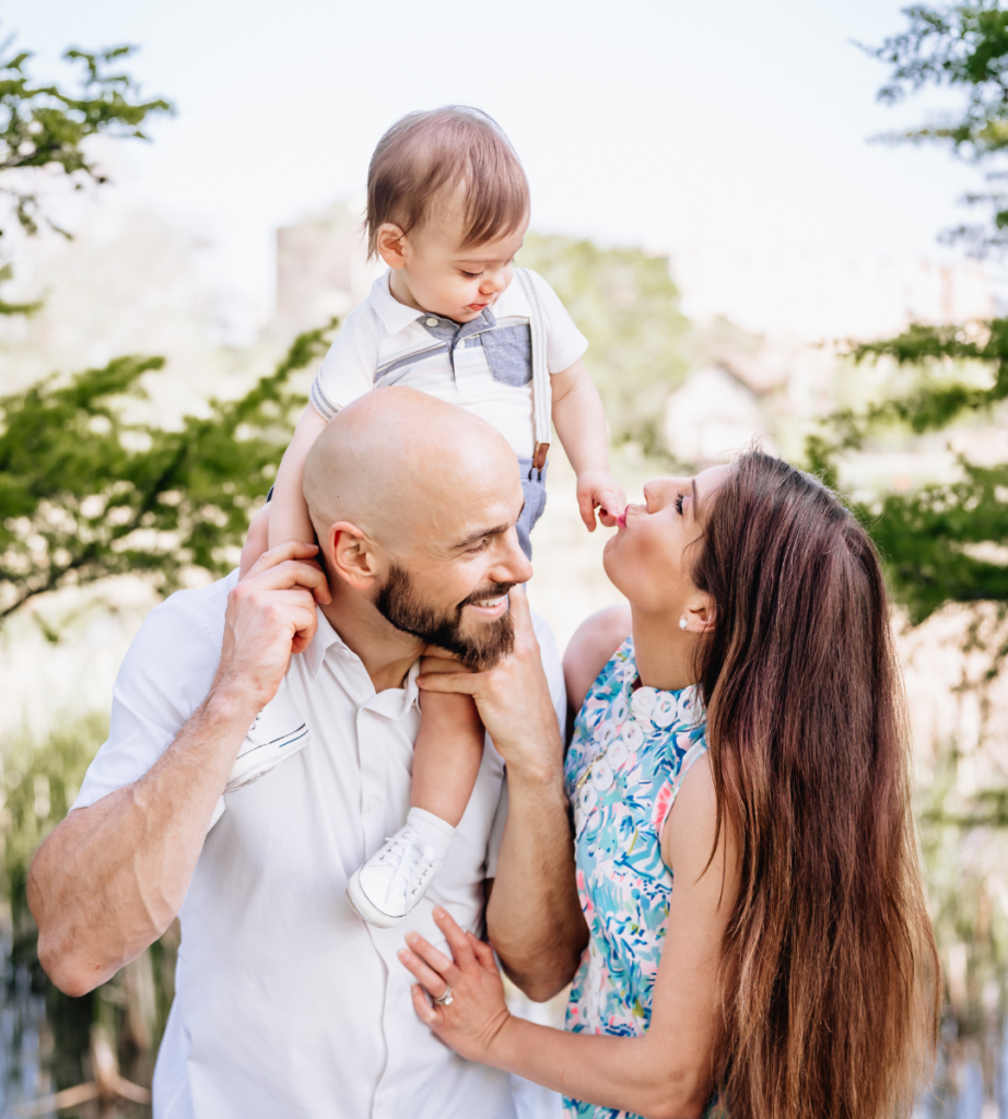 family of three with mother, father, and child on dad sholders