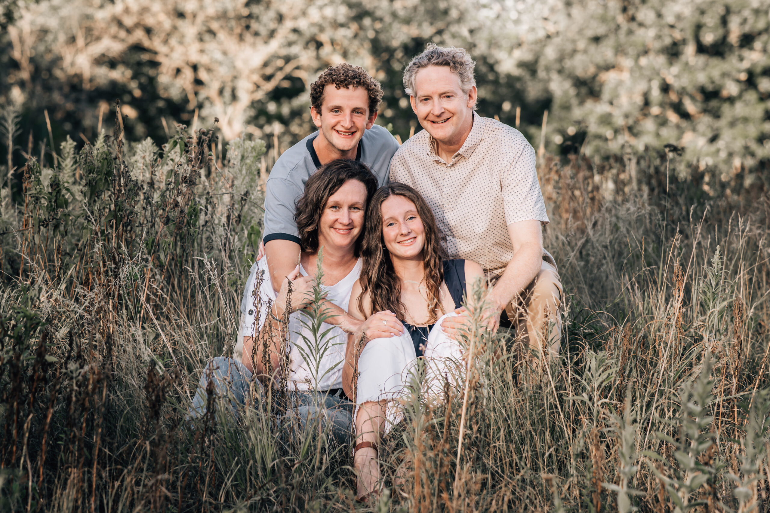 family of four sitting in tall grass together 