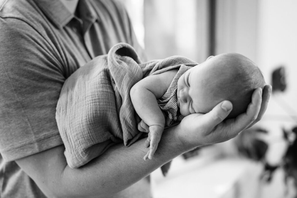 a newborn baby sleeping in the crook of an adult's arm