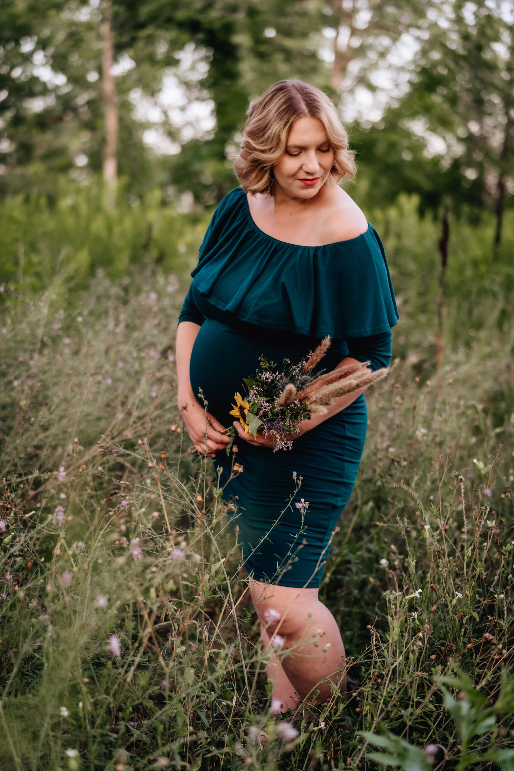 expecting mother in a field of grass holding wildflowers in her hands. 