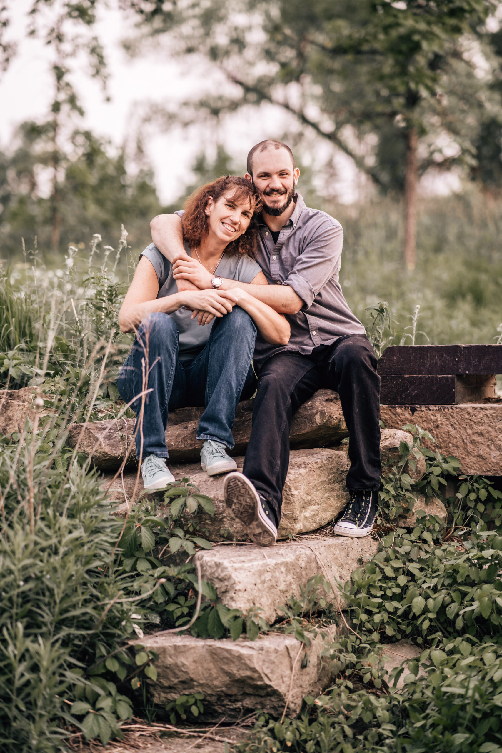 couple sitting on rocks - male has his arms wrapped around his partner's shoulders