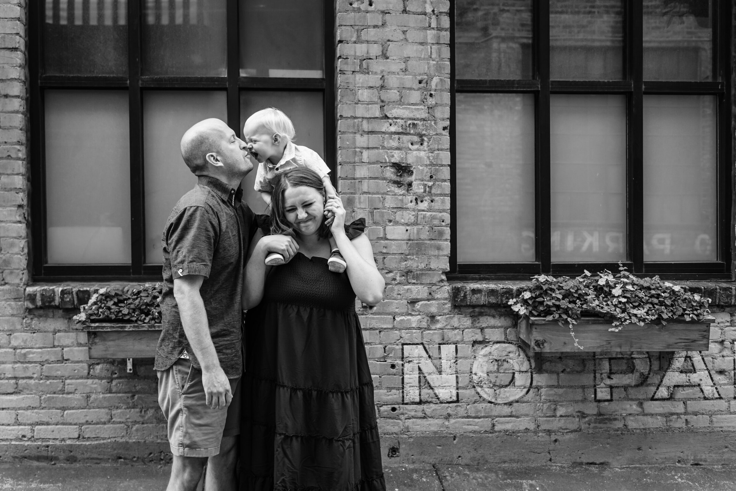 father kissing his toddler son while mother holds the toddler on her shoulders