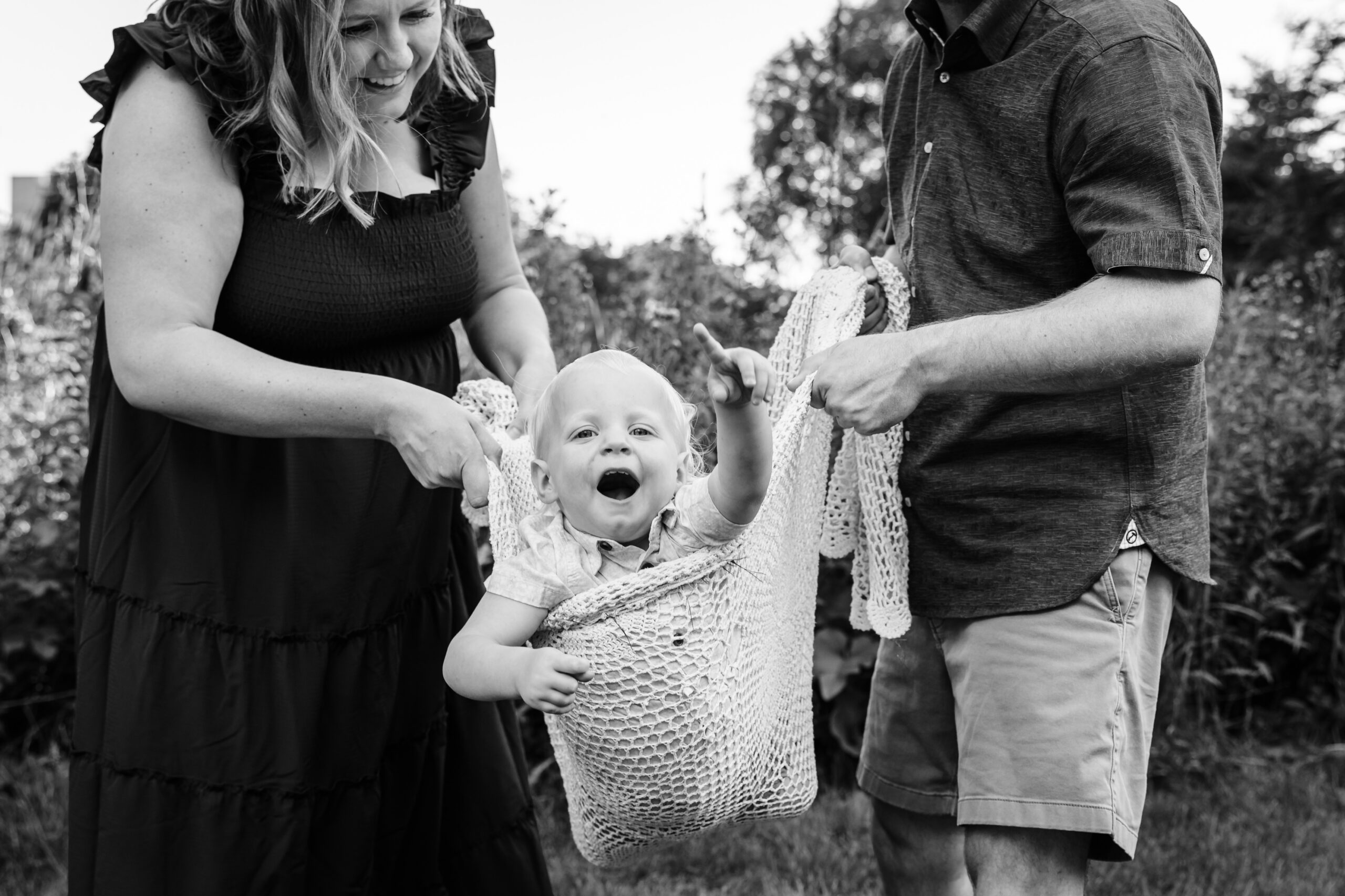 mother and father holding their toddle son in a basket between the two of them 