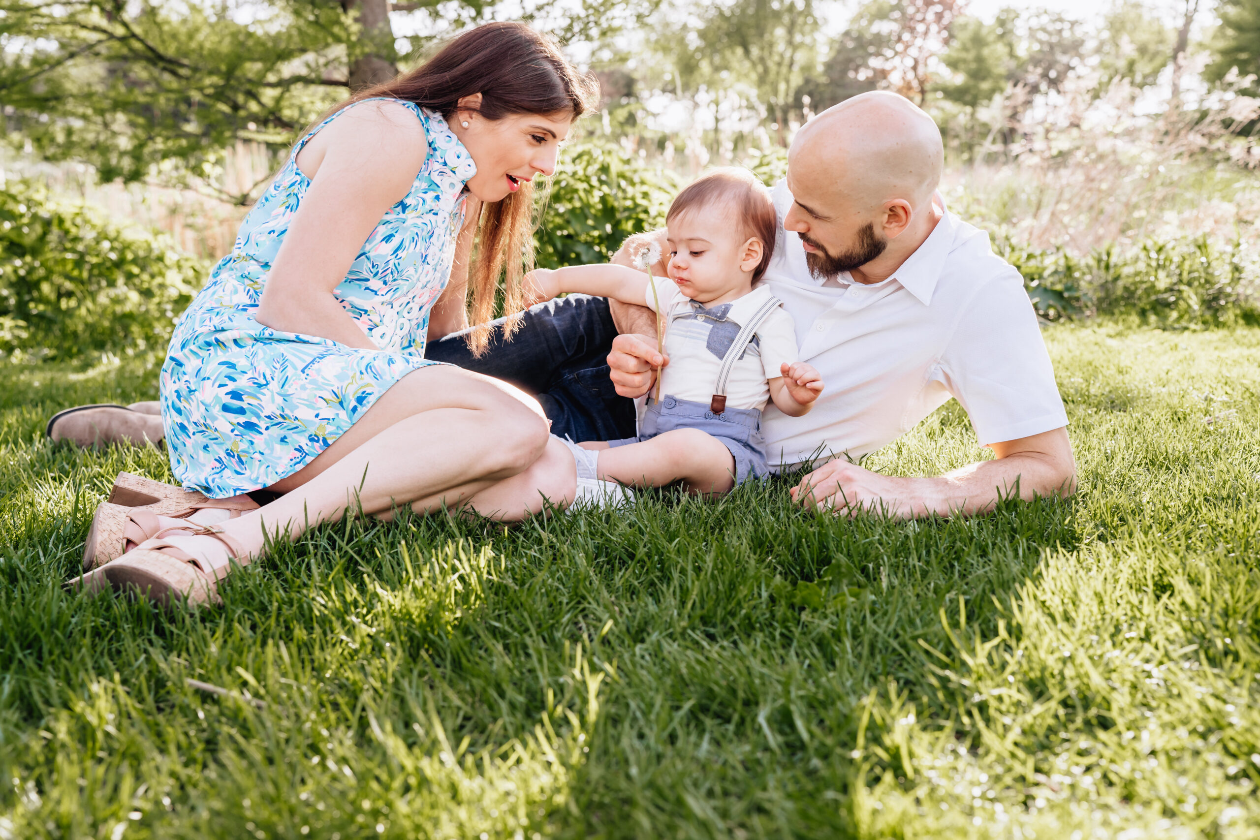 mother, father, and toddler son laying int he grass