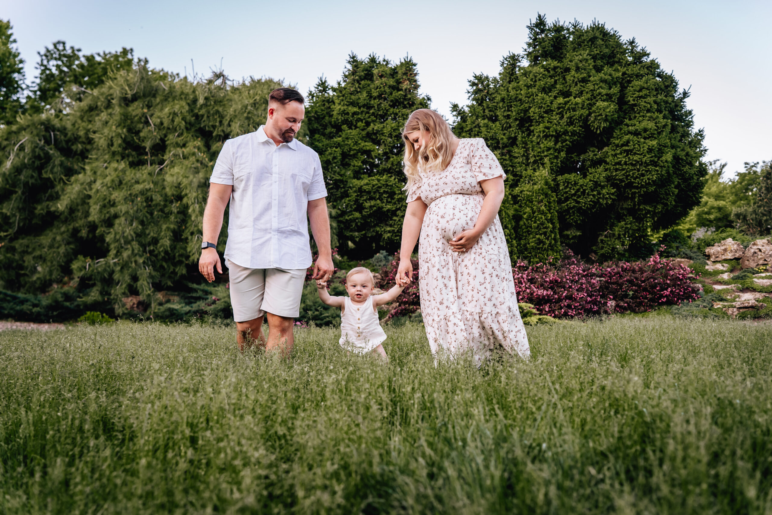 mother, father, and daughter walking in the grass holding hands 