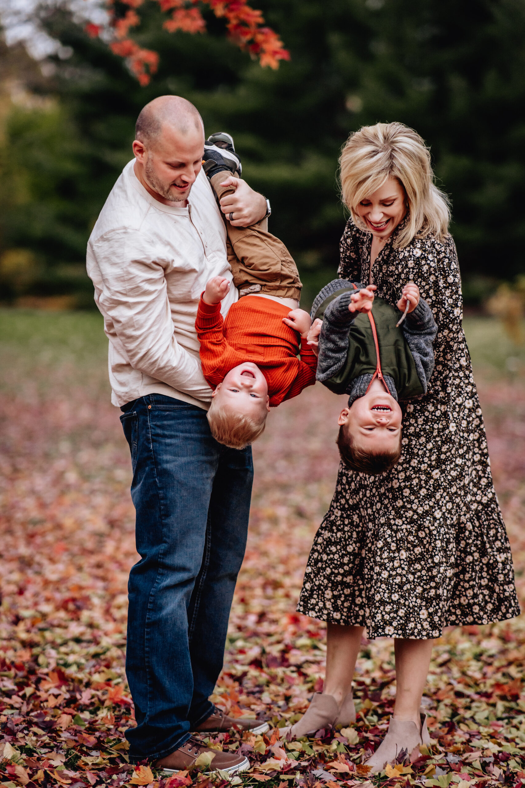 mother and father holding their two toddler sons standing under a tree 