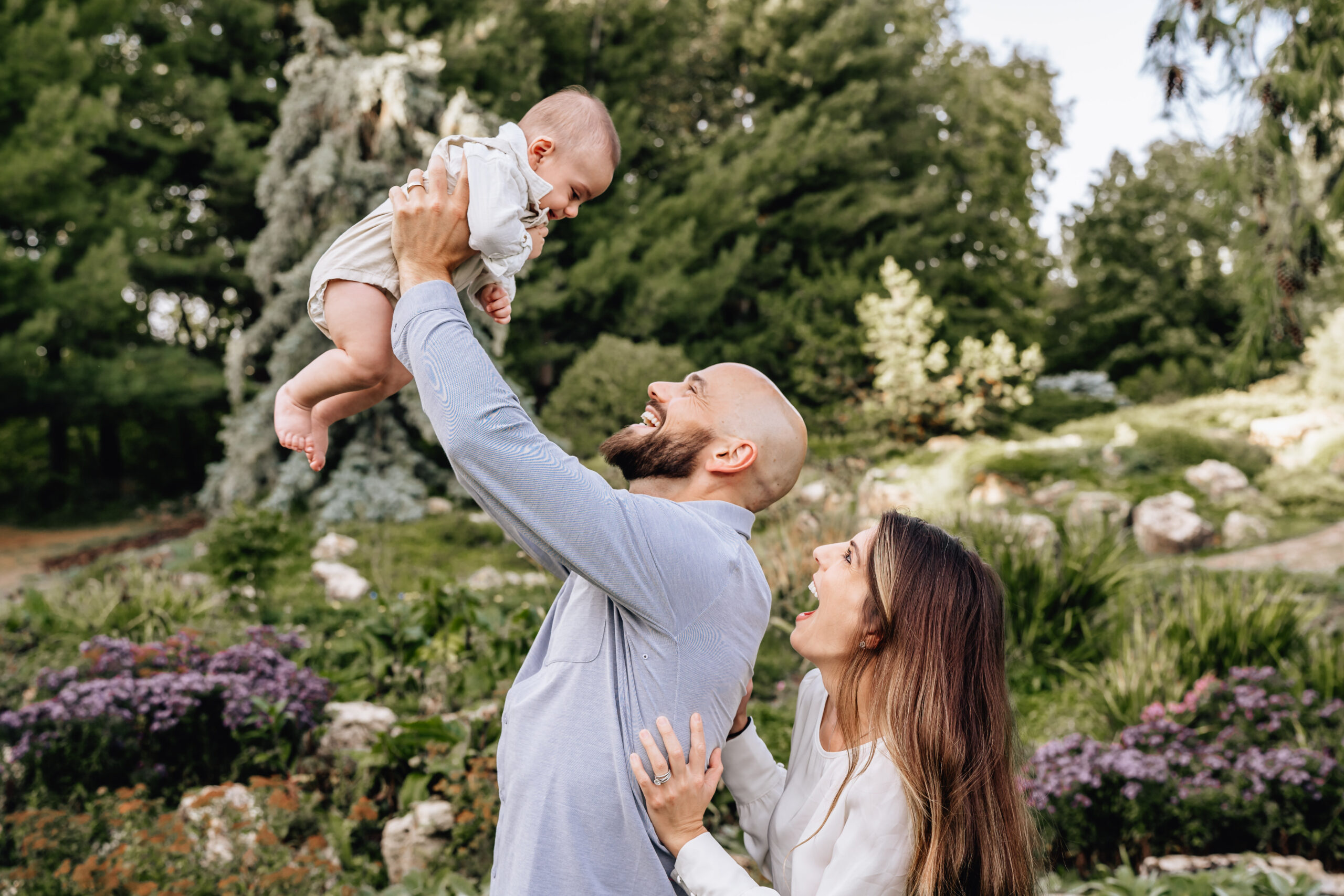 mother, father, looking at their baby while father lifts the baby in the air