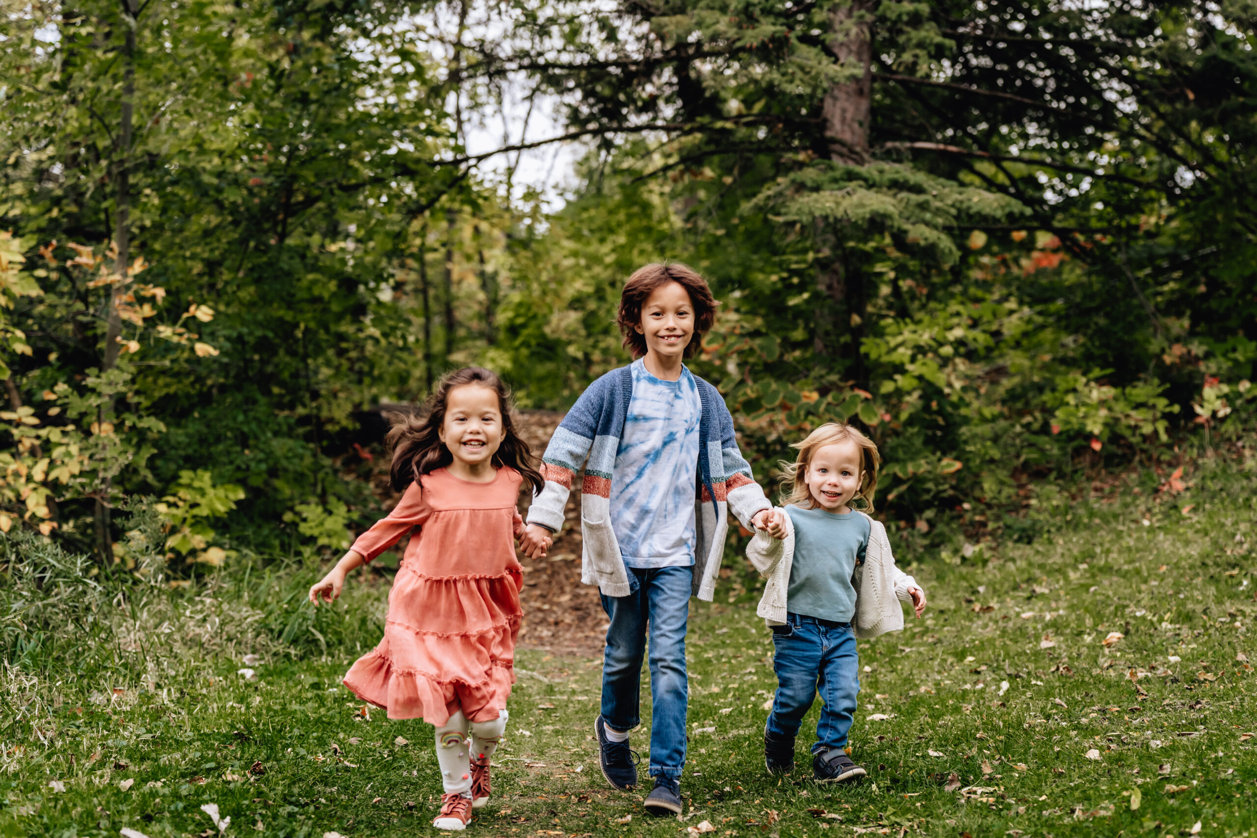 three sibling running towards the camera holding hands and laughing 