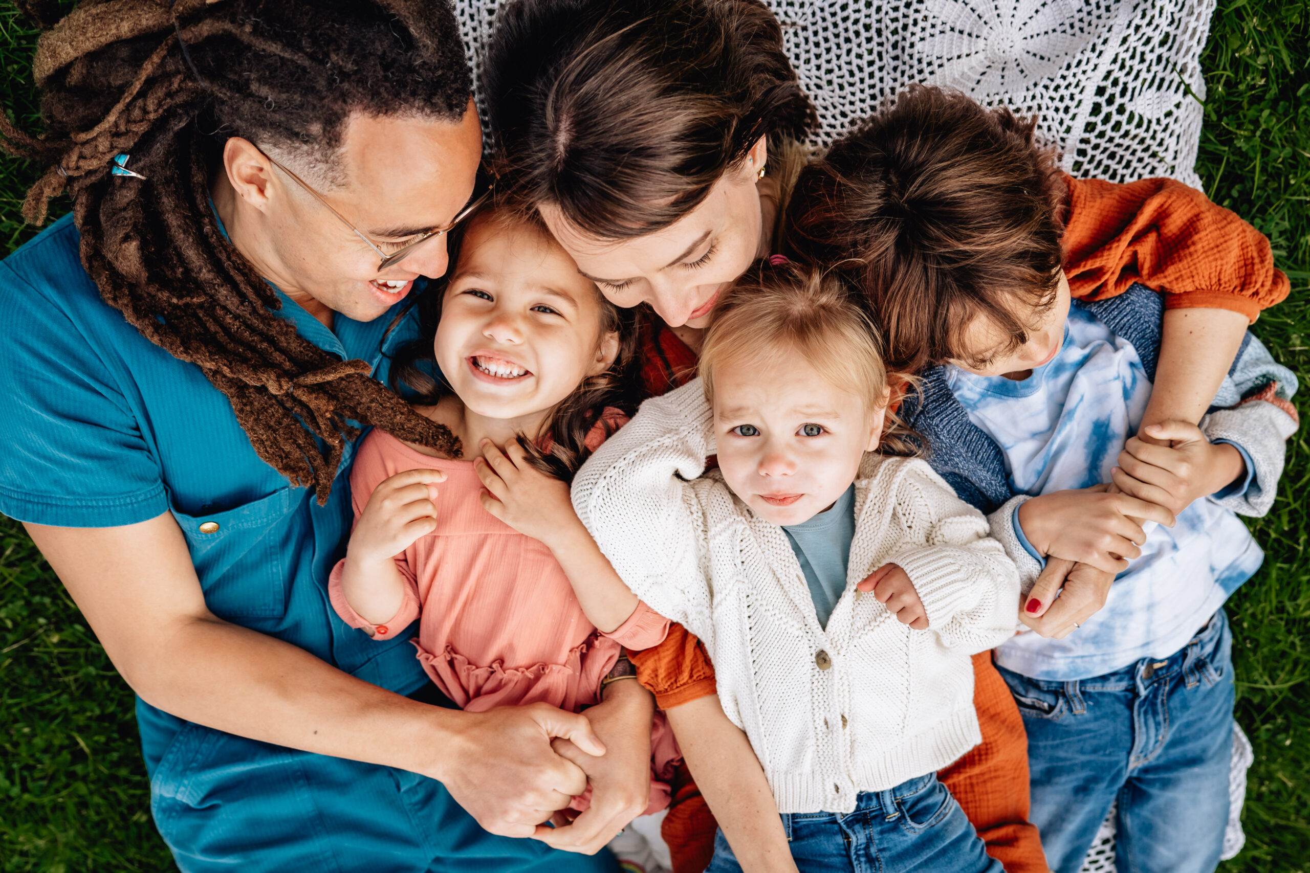 family of five laying on the grass together with mother and father looking at their children 