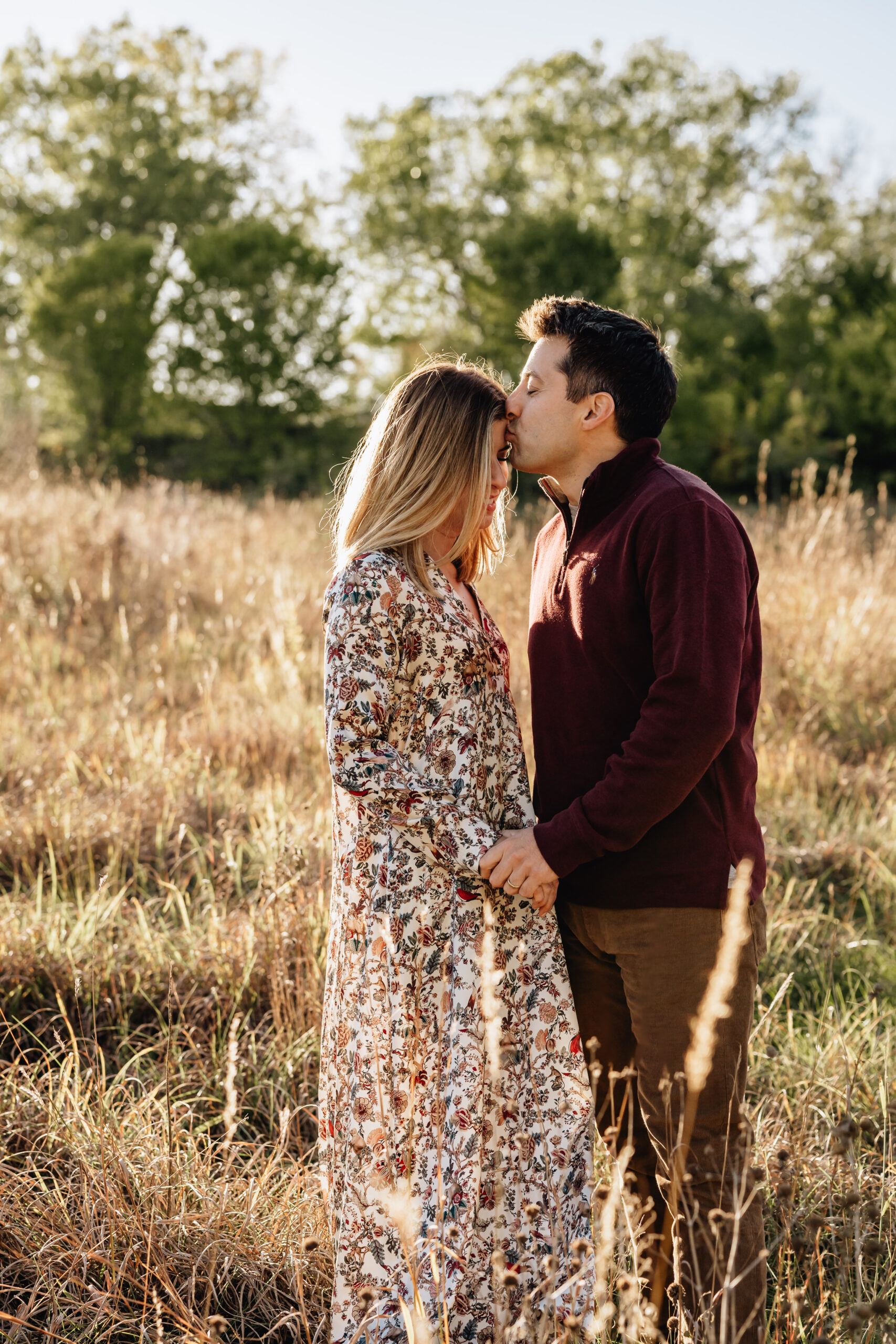 couple standinng in a field - male is giving his female partner a kiss on the forehead