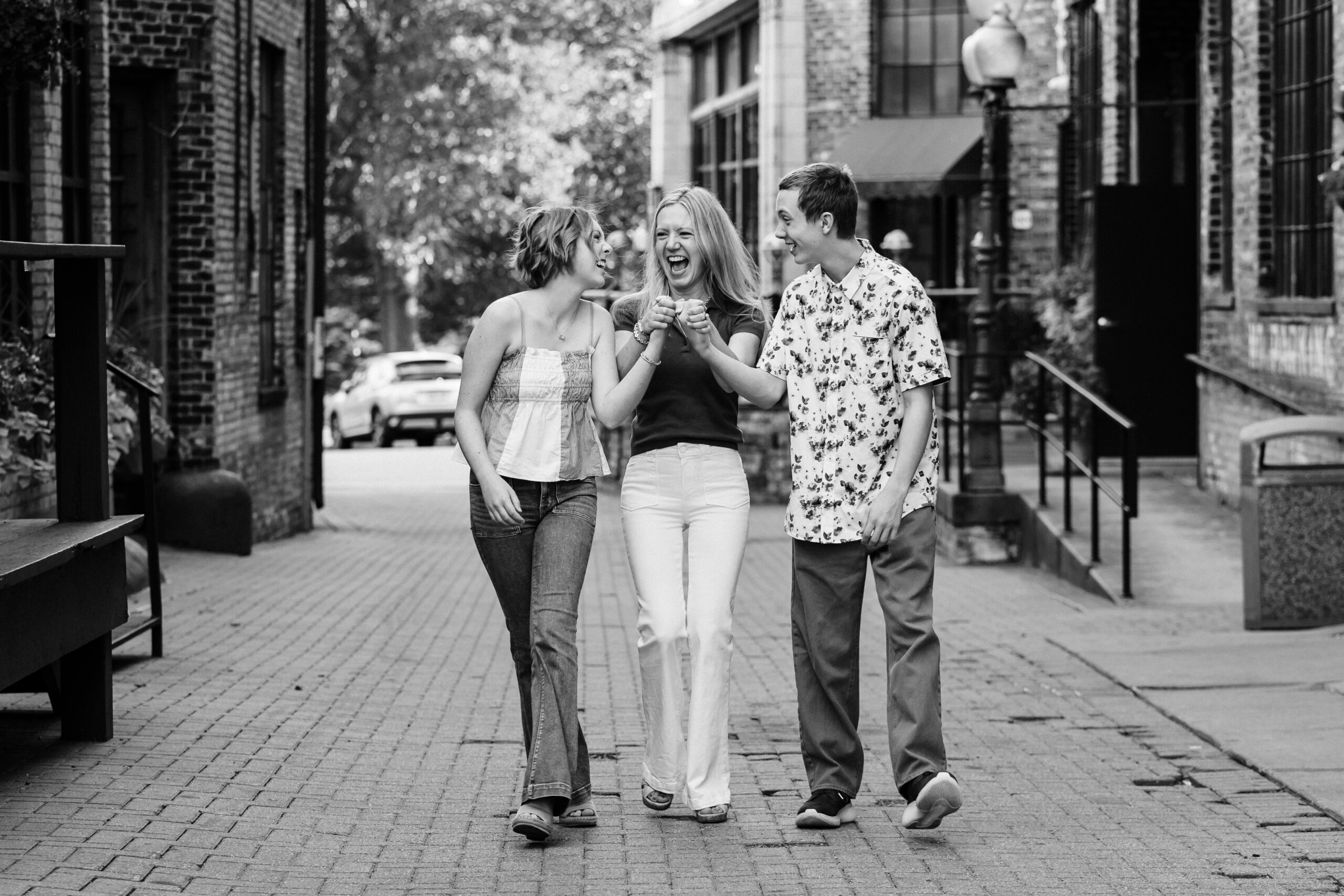 three siblings holding hands and walking down a street at Harmon Alley behind Café Lurcat, two sisters and one brother 