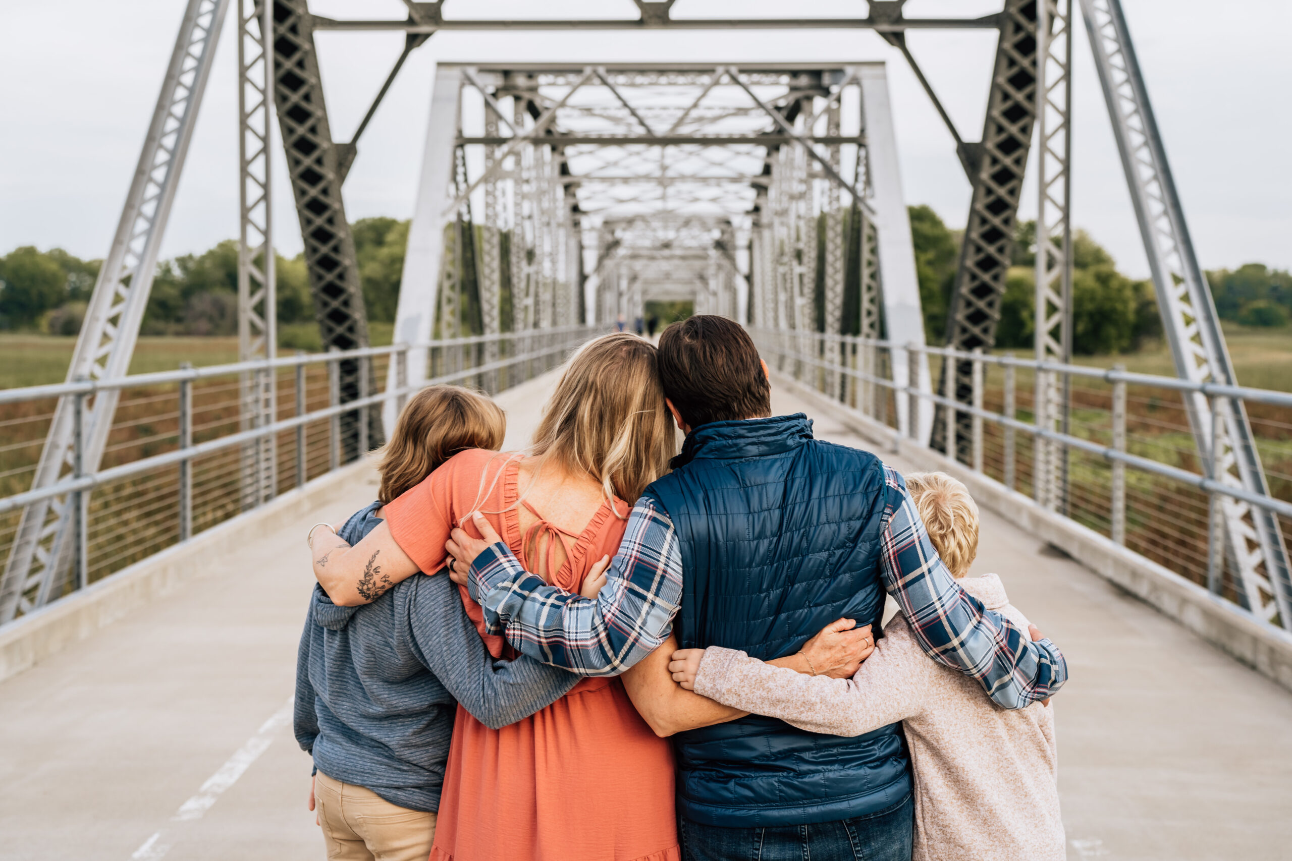 family of four standing on a bridge giving each other a hug. 