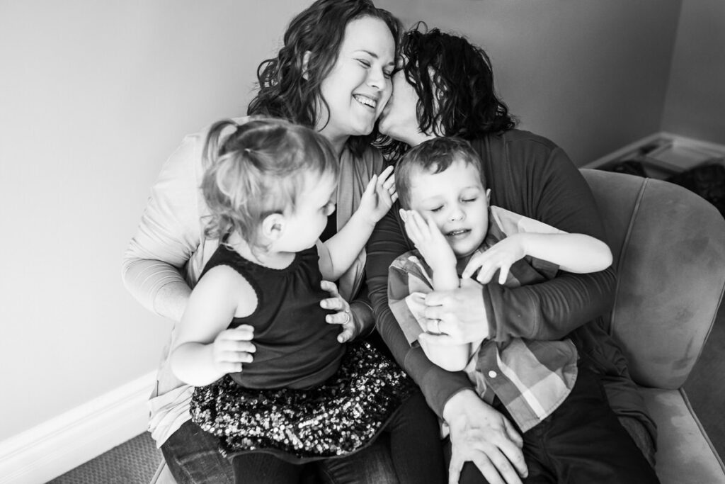 two mothers sitting on a chair with their two children, all smiling