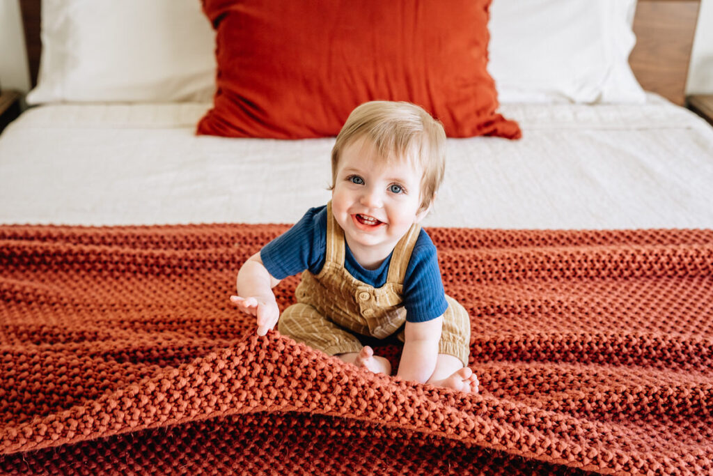 a baby sitting on a bed with a large orange knit blanket