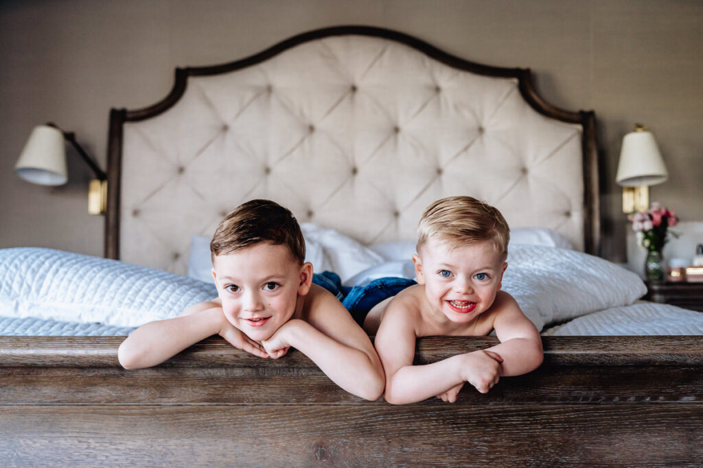 two young boys lying on a bed, smiling at the camera