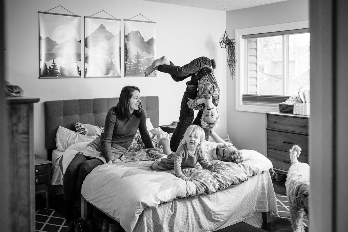 Parents sitting on a bed and playing with their kids during in home family photos