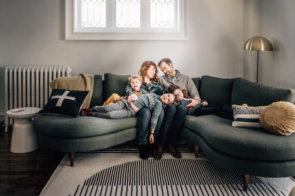 a family sitting on a couch, all snuggled together with the children lying on their parents' laps