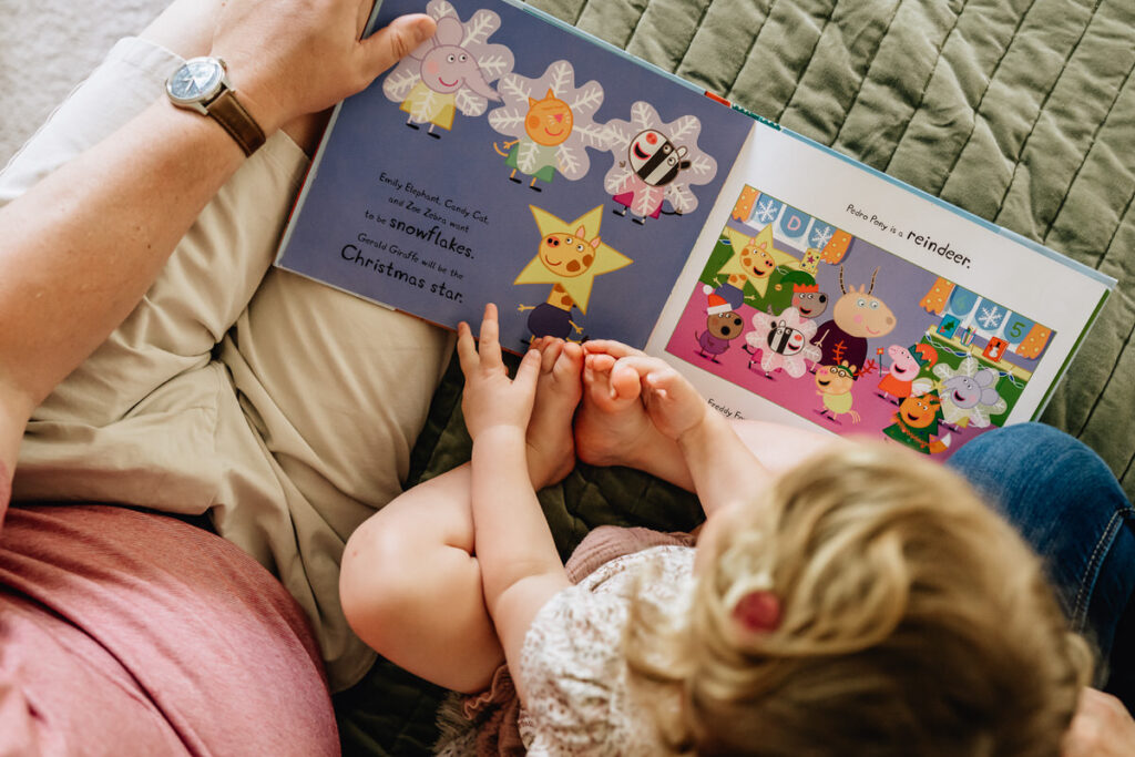 a child sitting on an adult's lap, reading a colorful children's book together