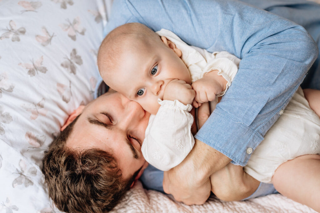 a father lying on a bed cuddling a baby who is sucking their thumb