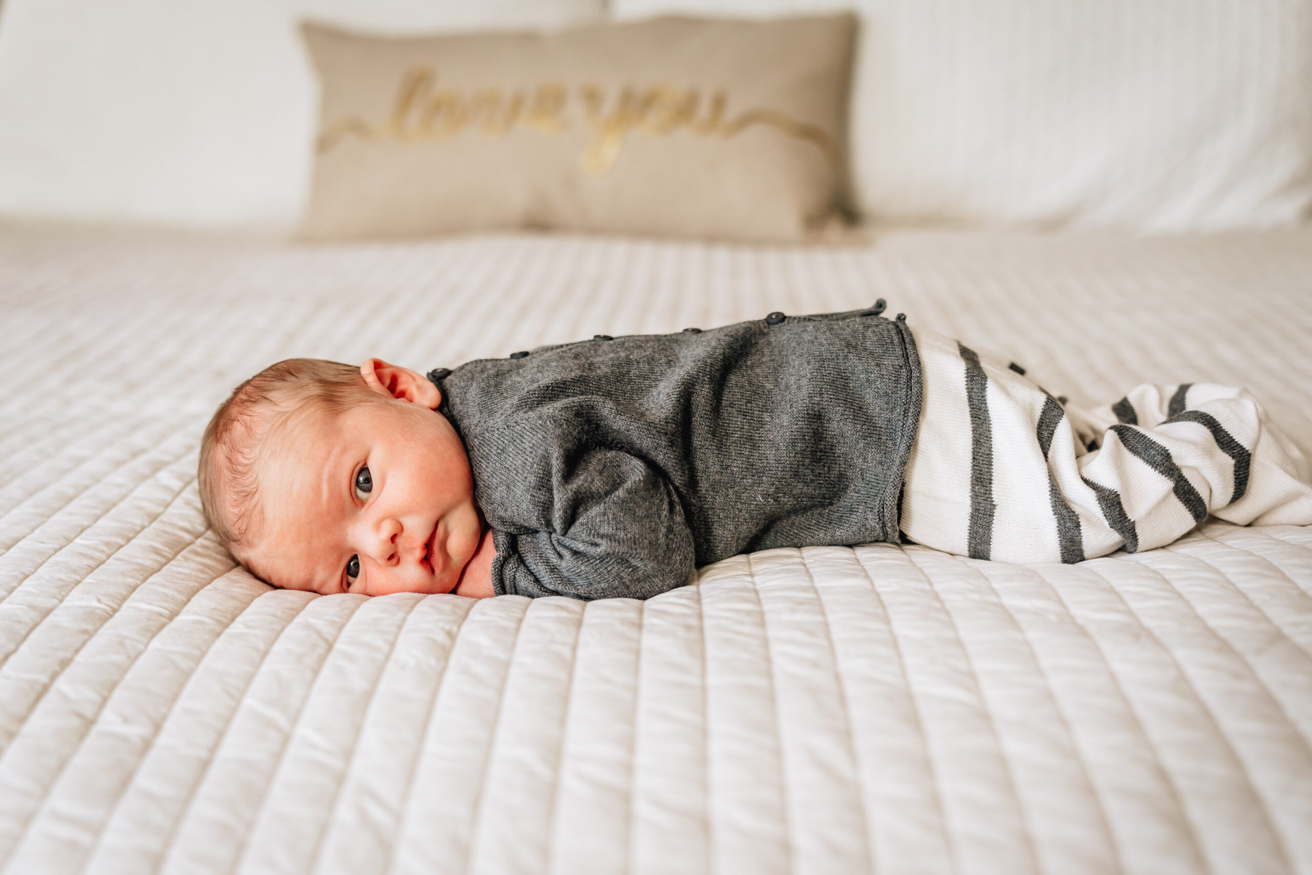 Newborn laying on a bed looking at the camera. 