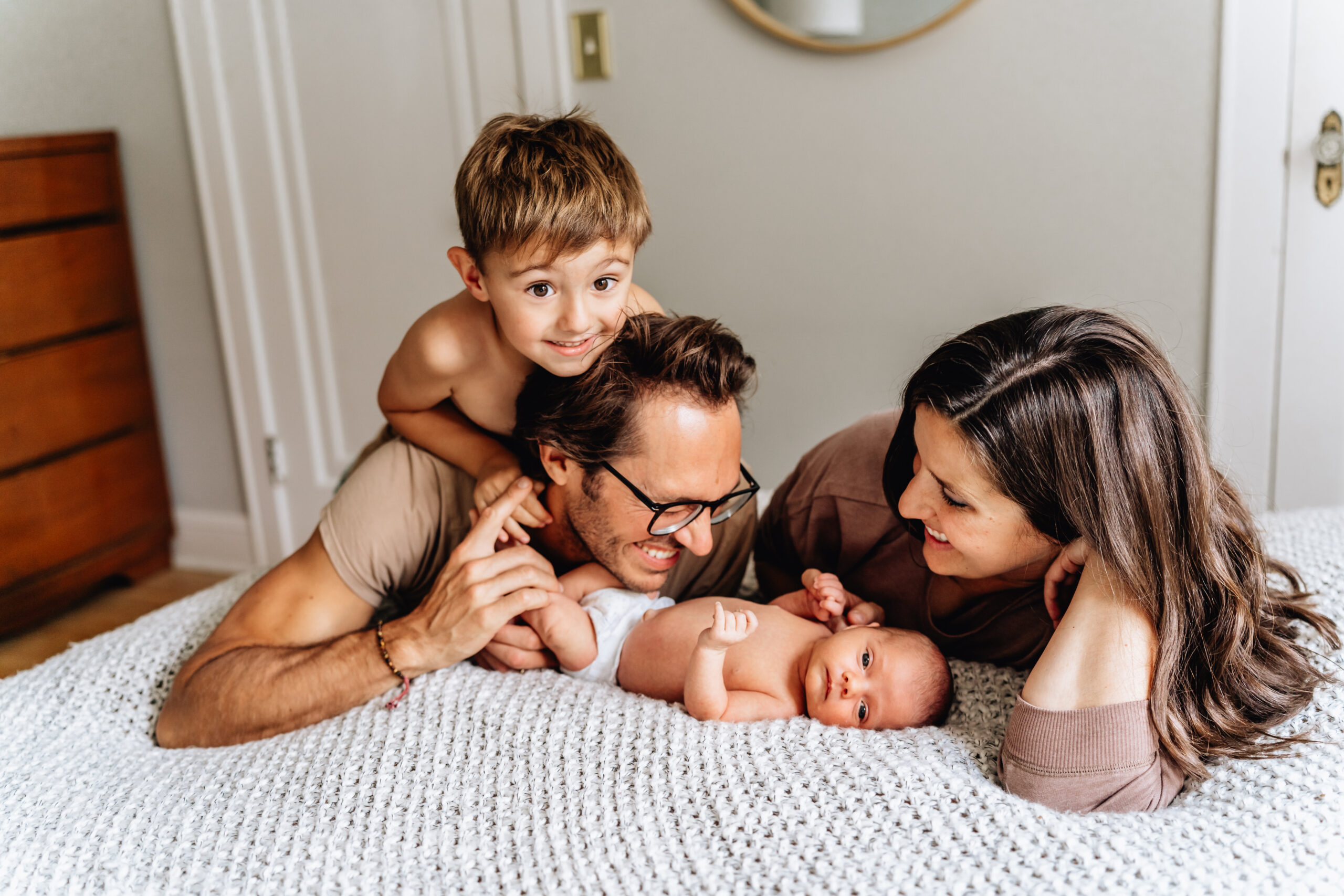 Family of four with a newborn baby. Mother and father are looking at newborn and older brother is playing with the father.