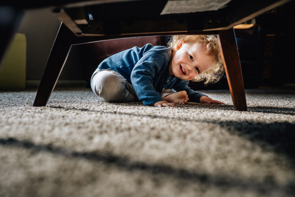 a young child smiling while crawling under a piece of furniture