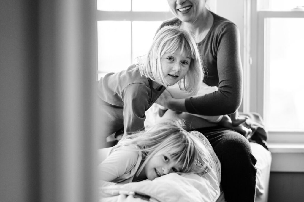 two young girls playing on a bed while their mother holds a newborn baby