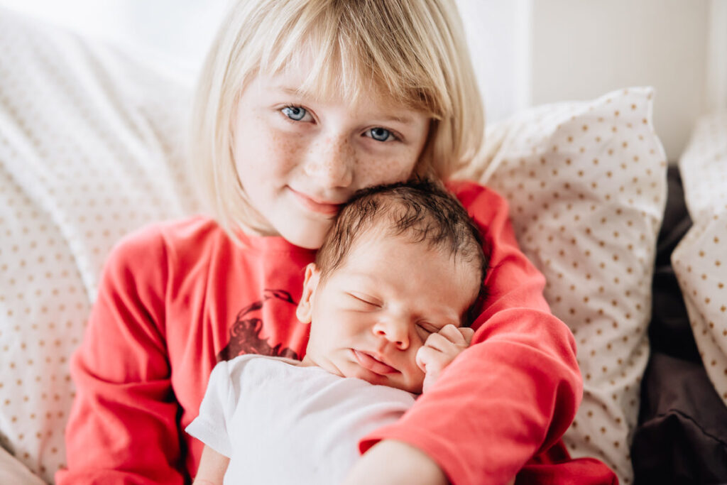 a young girl with blonde hair holding a newborn baby on her lap