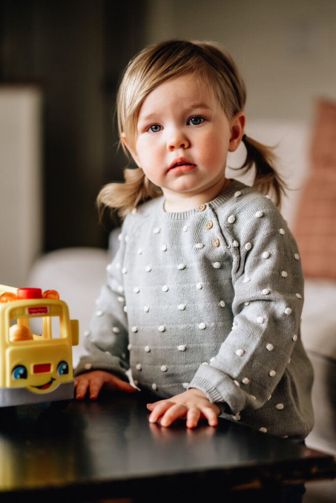 a toddler girl standing next to a toy bus