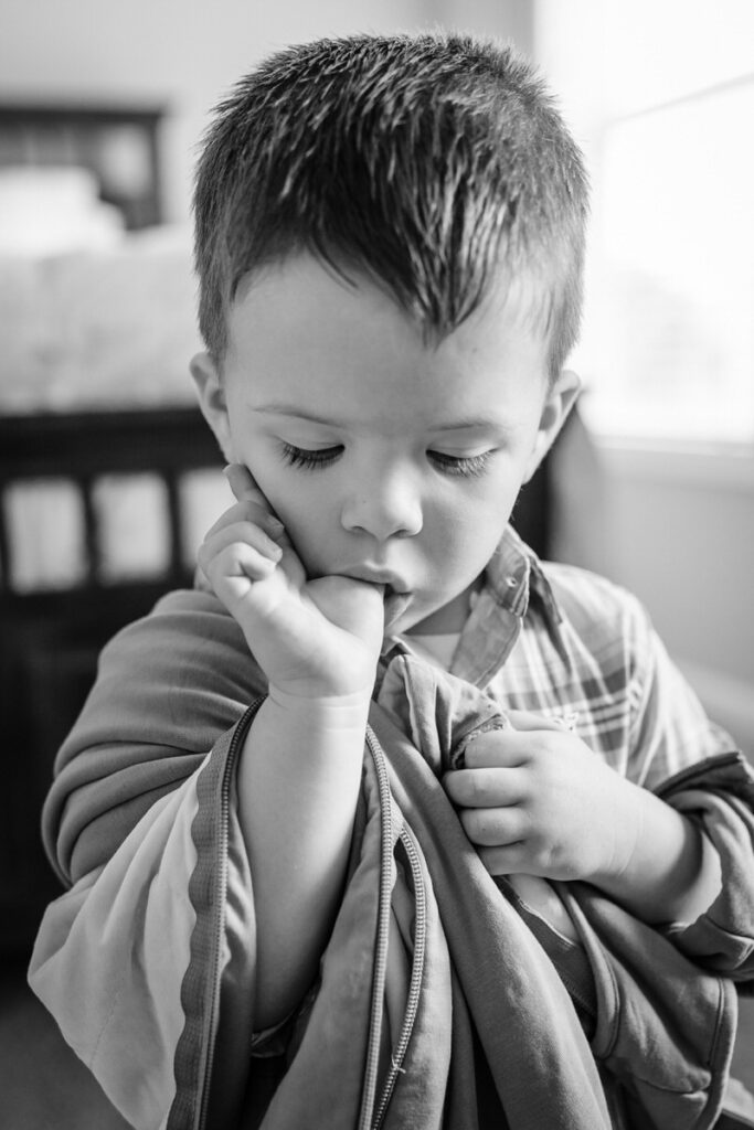 a young boy holding a blanket and sucking his thumb