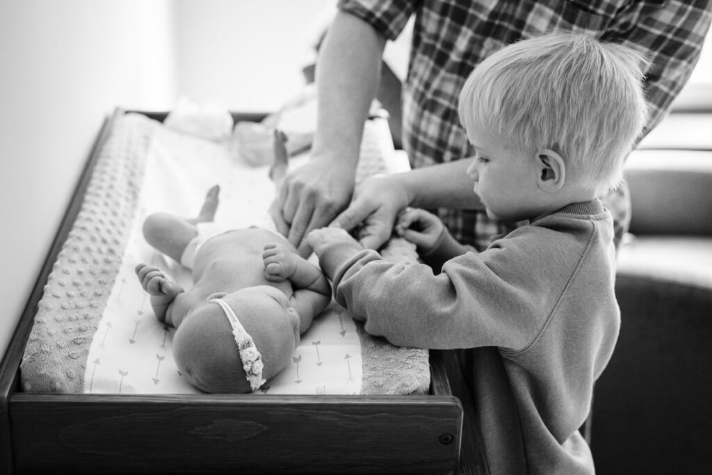 a young boy helping his father change the diaper of a newborn baby on a changing table