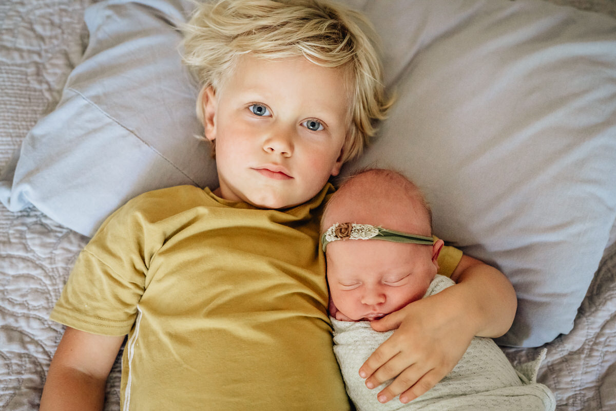 A young boy sitting laying down with their newborn sibling in their arms